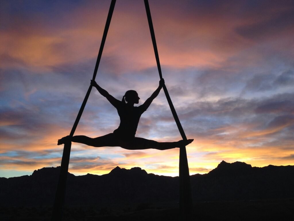 Silhouette of a person aerial yoga against a sunset sky.