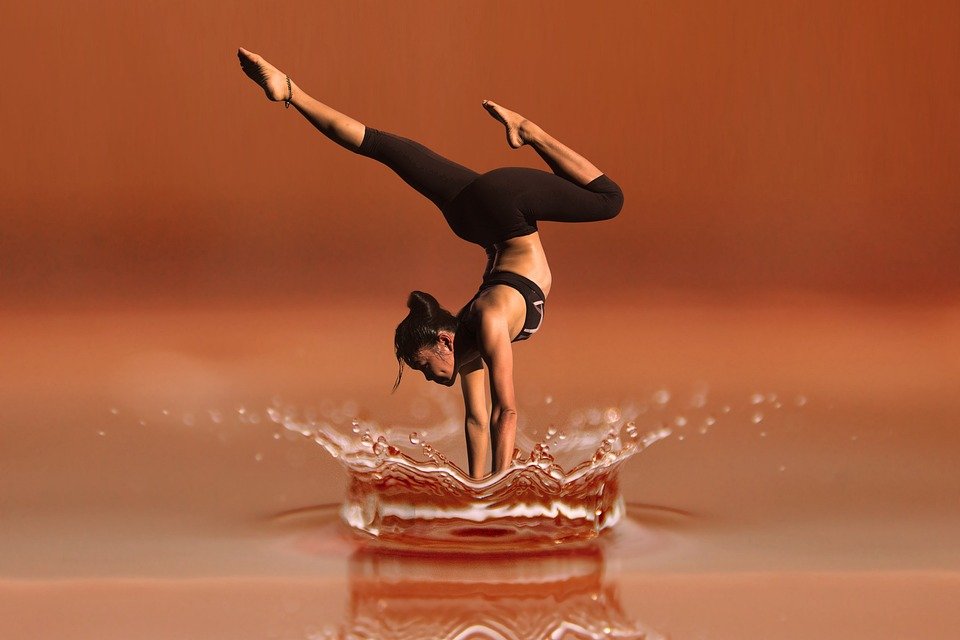 A woman gracefully balances on her hands, appearing to touch the surface of a large splash in a serene, warm-toned environment.