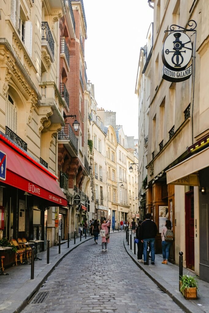 People walking down a charming, narrow street lined with Parisian cafes.